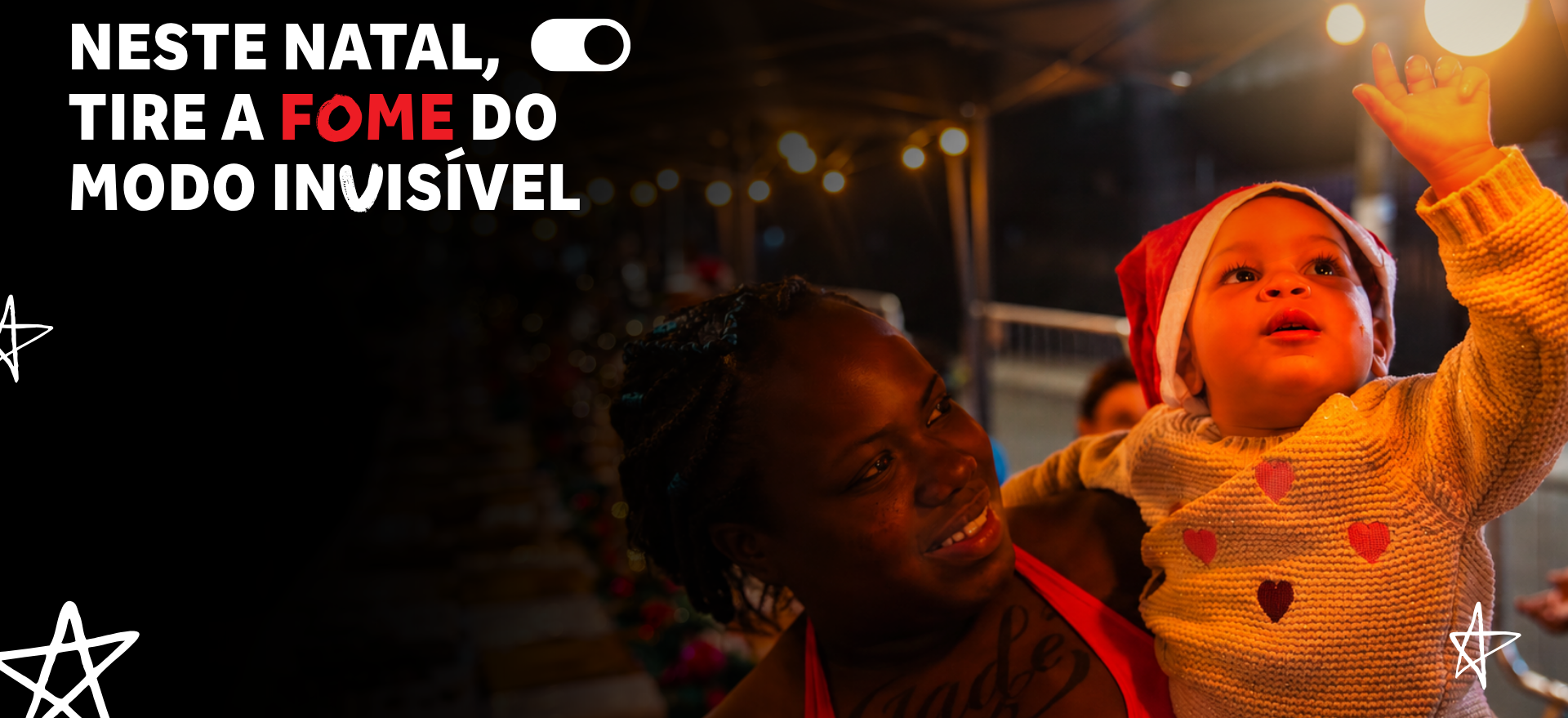 Mãe sorri segurando bebê com gorro de Papai Noel que estende a mão para uma luz, na campanha Natal Invisível da SP Invisível.