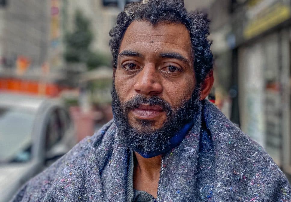 Retrato de homem em situação de rua, usando cobertor para se aquecer